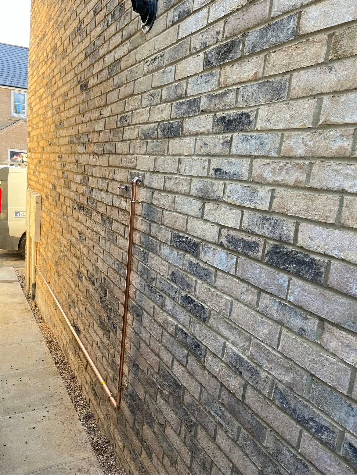 External gas and water pipework run neatly along a brick wall